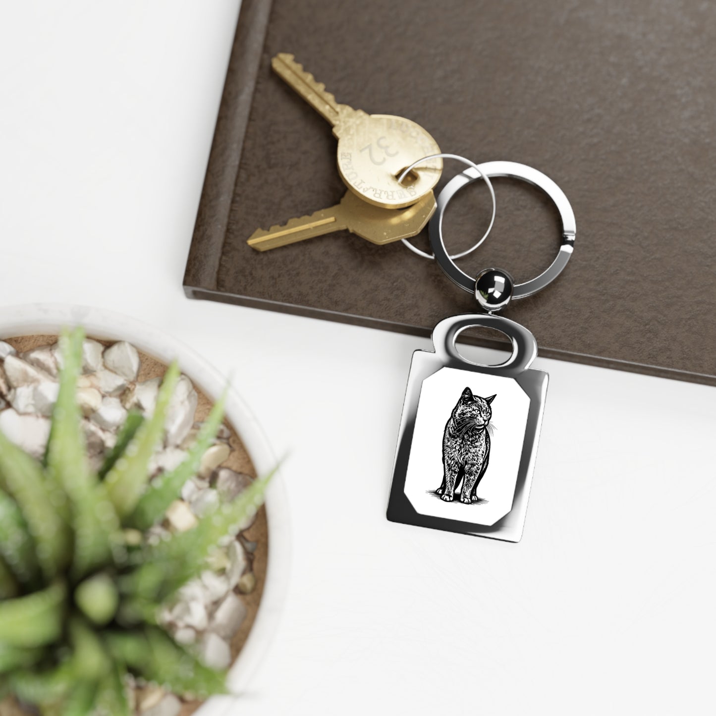 Keychain with a cat design on a surface with a key and plant.