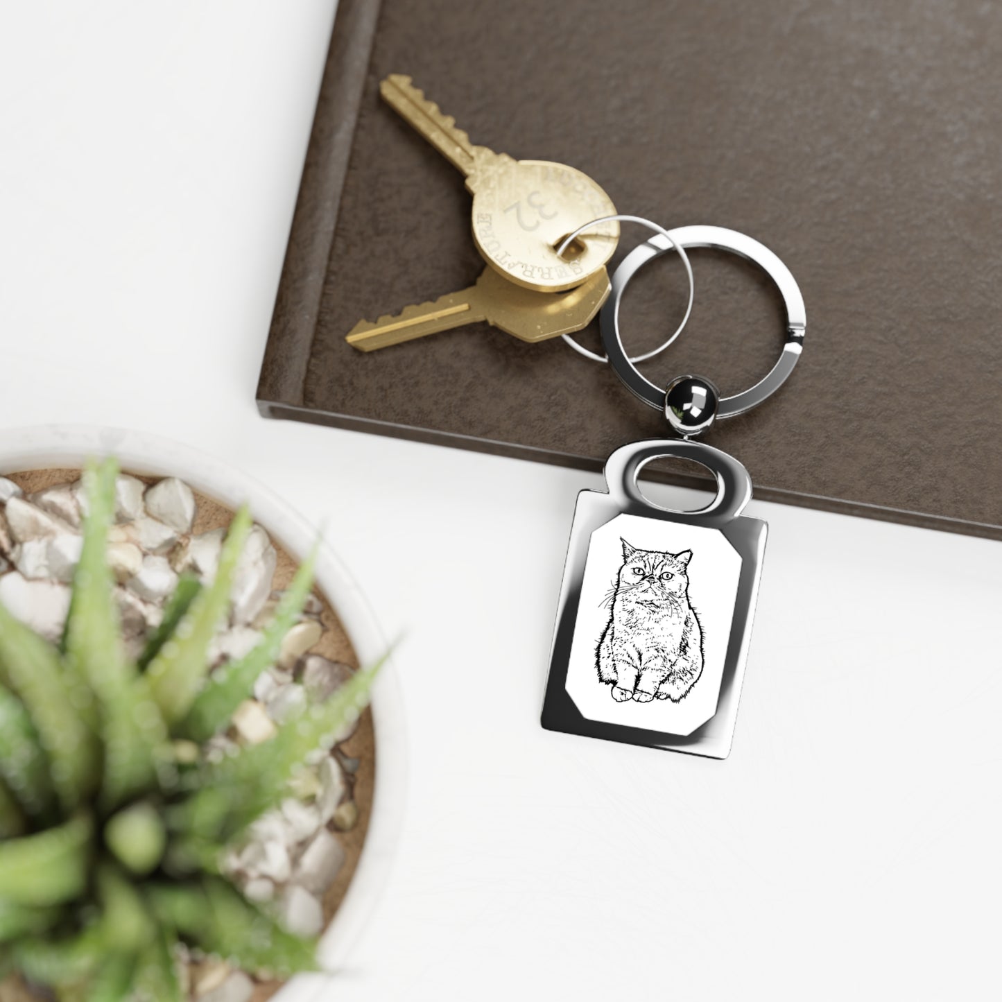 Keychain with owl design on a keyring, placed on a surface with a plant and notebook.