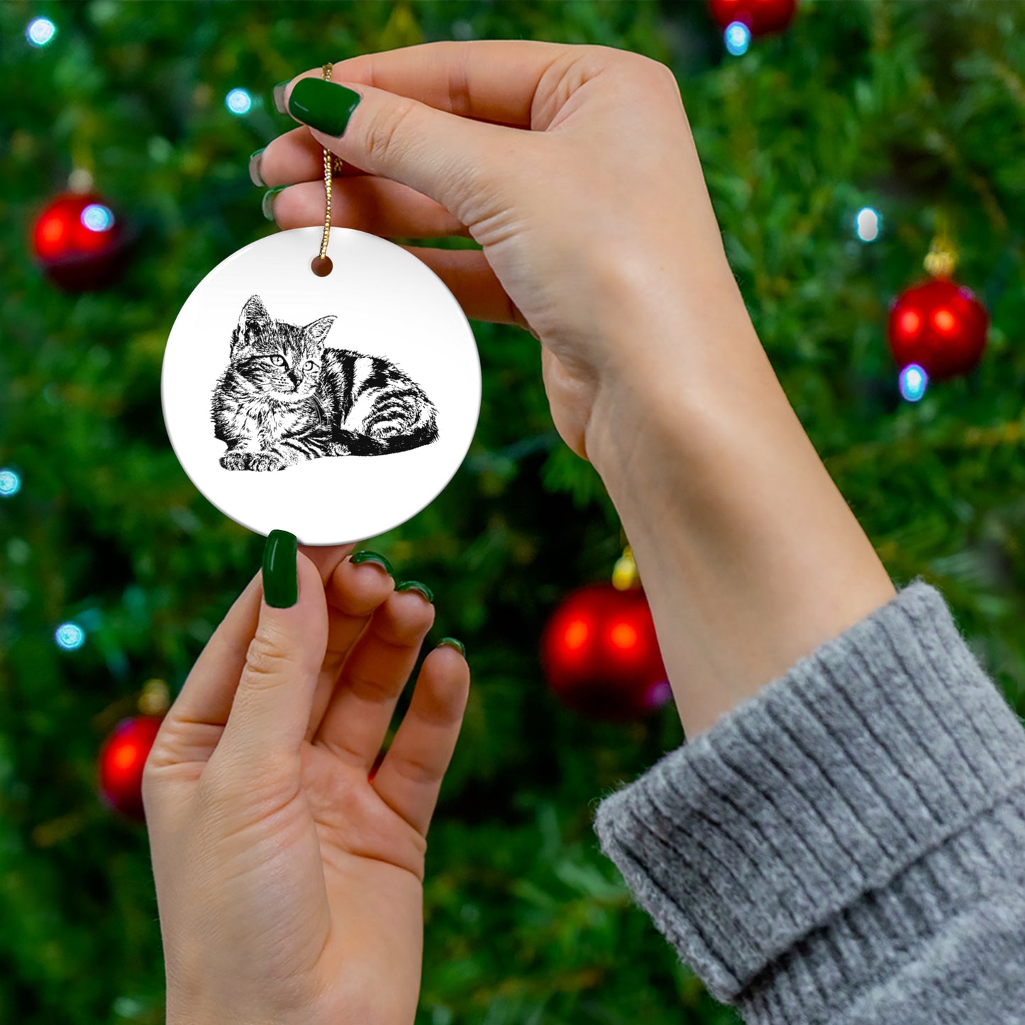Hand holding a circular ornament with a cat design against a Christmas tree background